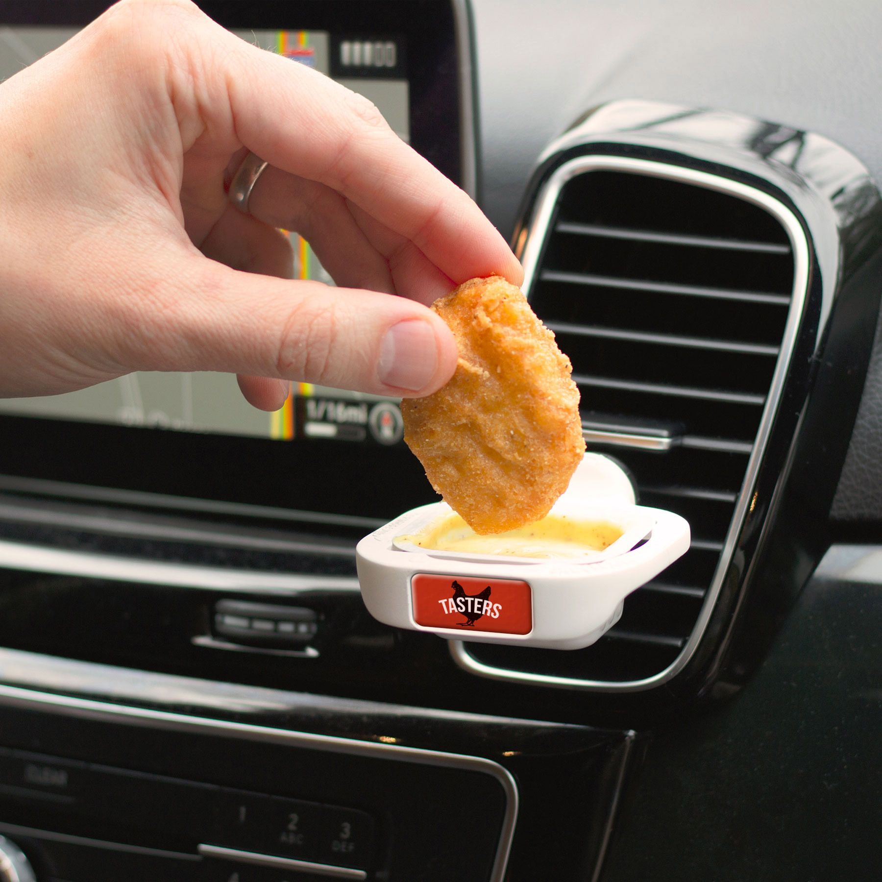 hand dipping a chicken nugget into sauce with a clap attached to a car vent